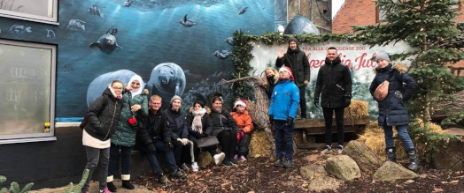 En flok unge står i varmt vintertøj i Zoologiske Have i Odense foran et blåt murmaleri
