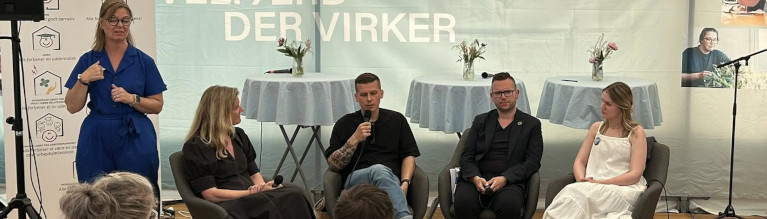 Et panel på fire personer sidder på en række og taler i et telt på Folkemødet