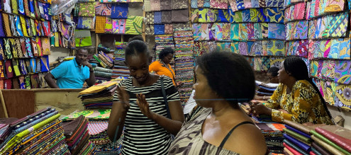 To afrikanske kvinder står og taler foran farvestrålende tekstiler, der ligger fra gulv til loft på hylder