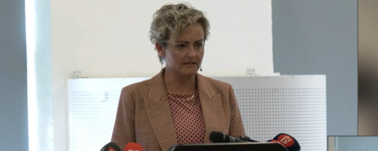 Social- og boligminister, Pernille Rosenkrantz Theil, står på en talerstol med mikrofoner foran sig.