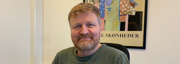 Nærbillede af Ole Wøssner, ny chef for CFD Rådivning. Han sidder foran en abstrakt plakat, hvor der står skønheder lige i Oles hovedhøjde.