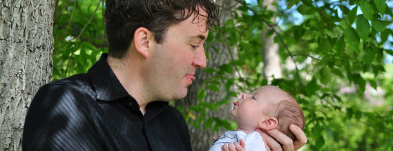 En far holder sin baby tæt på ansigtet. De efterligner hinandens grimasse.
