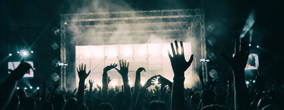 Sort hvis billede fra en koncert hvor en masse hænder er i luften. Lys på scenen.
