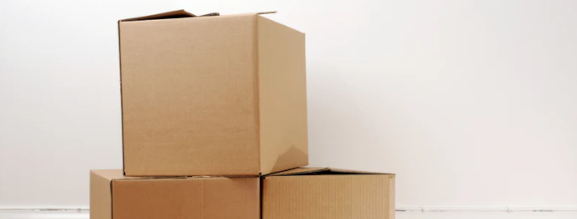 Flyttekasser, der står ovenpå hinanden op ad en hvid væg.