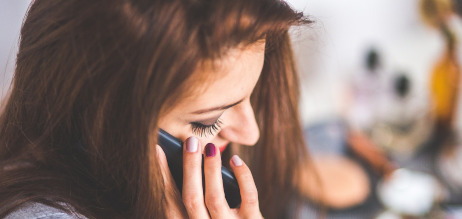 En ung kvinde sidder i profil og tale i mobiltelefon. Hun ser ned og ser lidt trist ud.