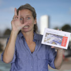 En kvinde i en blå skjorte laver tegnet for CFD med den ene hånd og holder et postkort i den anden hånd.