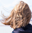 En ung kvinde står med ryggen til - hendes skulderlange hår blæser i vinden