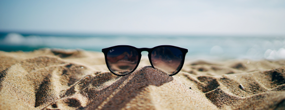 Foto af solbriller i sandet på en solbeskinnet strand.