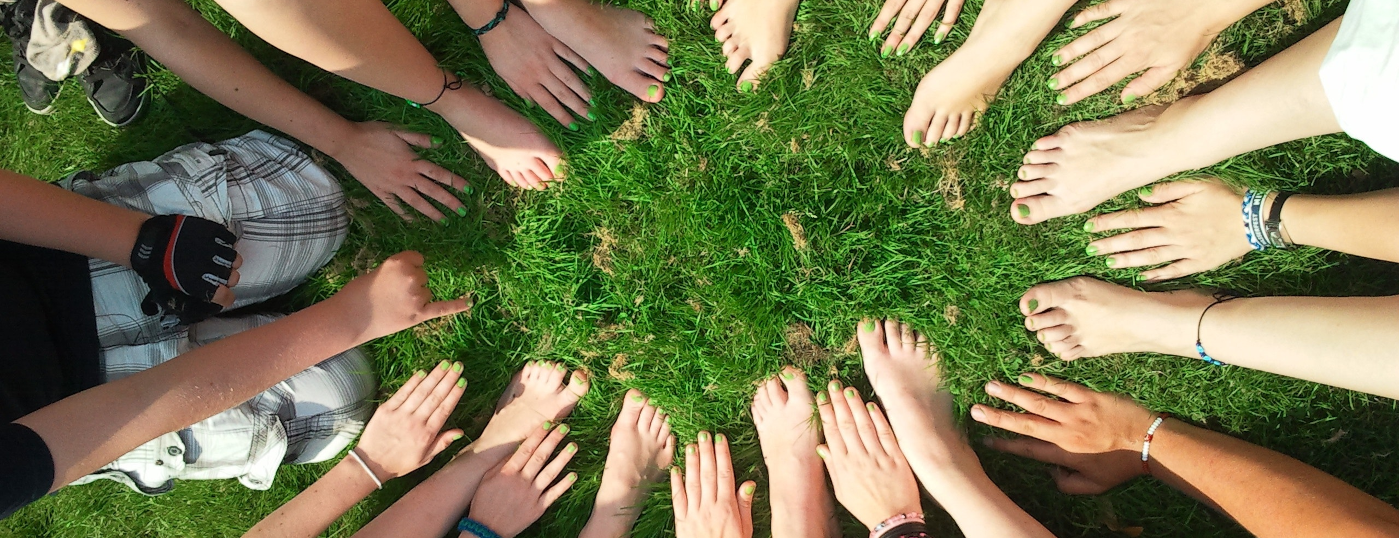 En gruppe unge med hænder og fødder i en rundkreds på græsset - en af dem viser kun en finger.