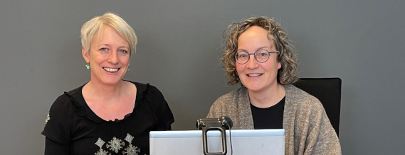 To kvinder (Rikke og Karin) sidder ved en computer og smiler til fotografen