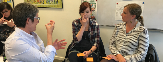 Billede der viser tre siddende kvinder, der taler tegnsprog med hinanden.