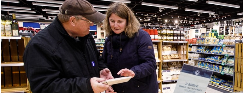 Kvinde og mand står ved en køledisk i supermarked og kigger på en vare
