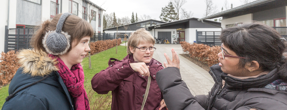 Tre unge kvinder står udendørs på CFD og taler sammen på tegnsprog en kølig efterårsdag.