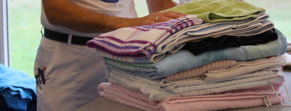 På billedet ser du en bunke håndklæder, som er lagt sammen og en krop, der står lige bagved iført hvide arbejdsbukser.